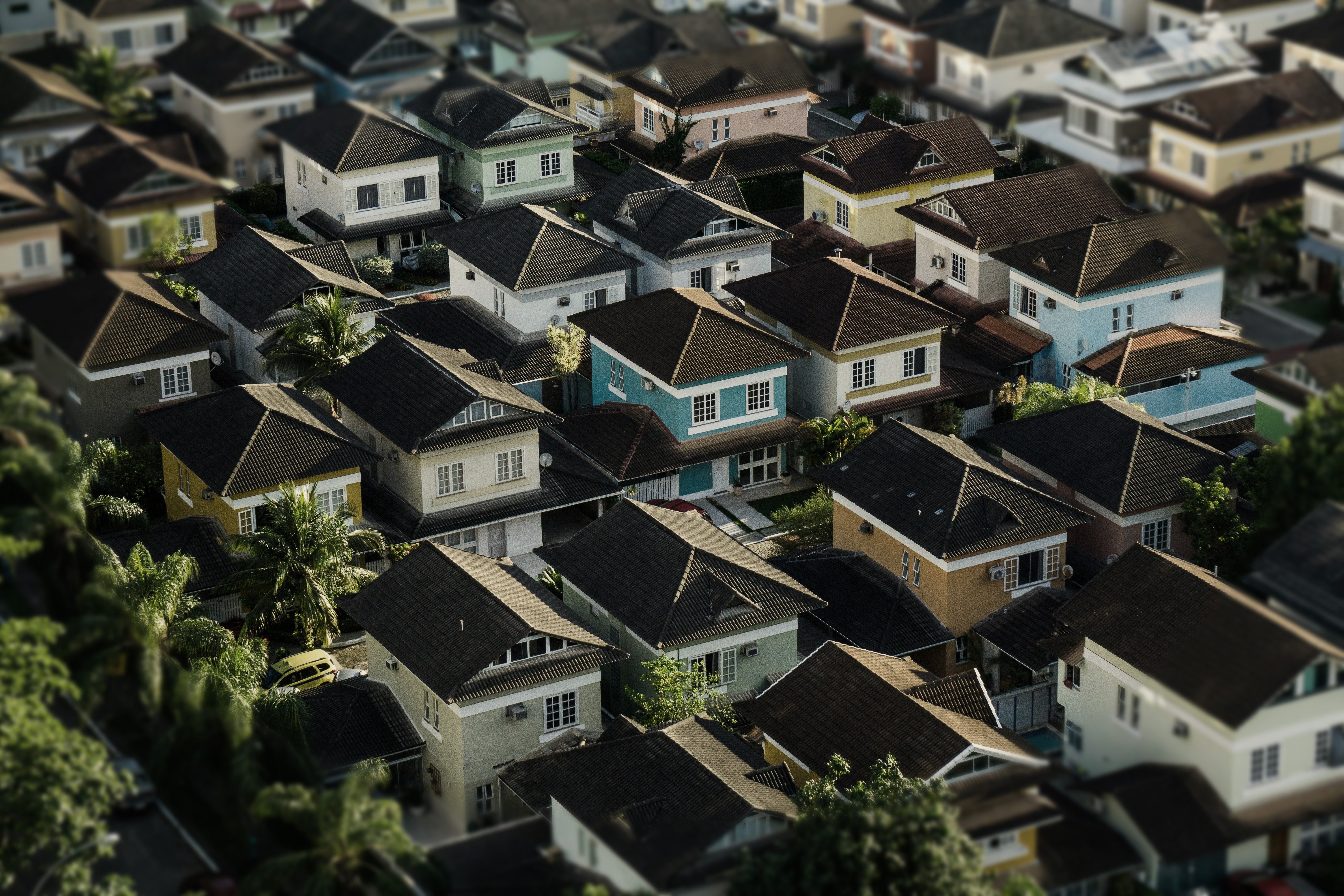 Aerial view of a dense suburban neighborhood with closely packed, colorful single-family homes featuring dark tiled roofs and small yards surrounded by palm trees.
